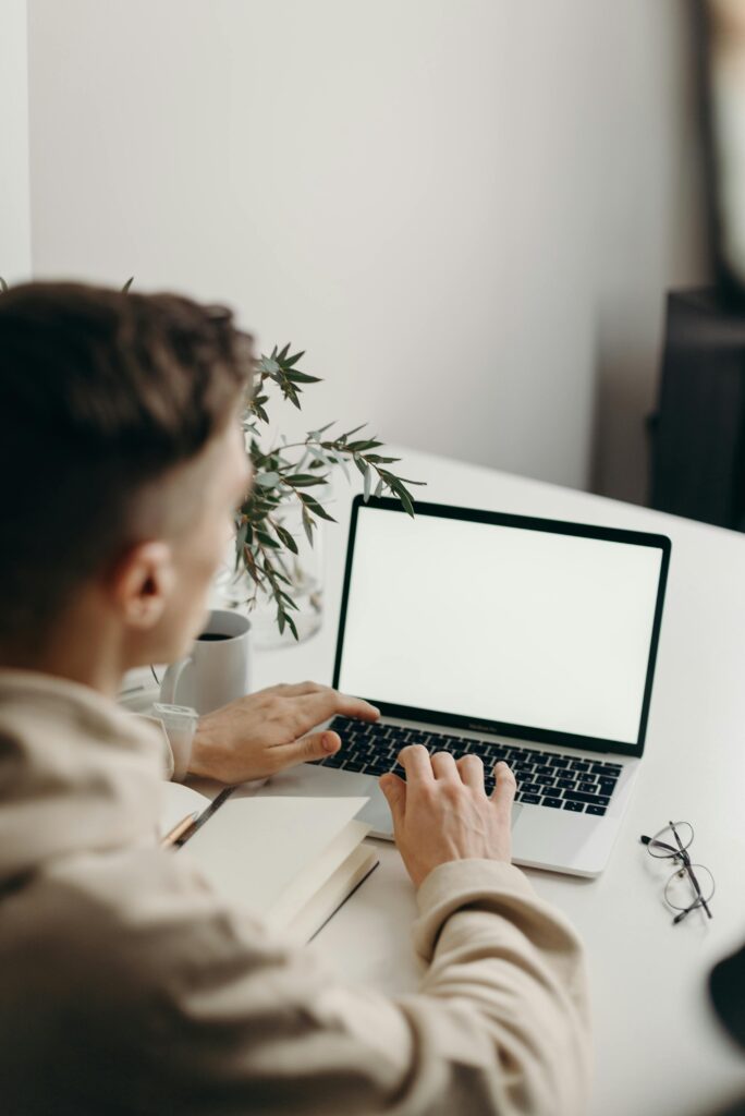 Young man typing on a laptop at a clean, minimalist desk with a plant.